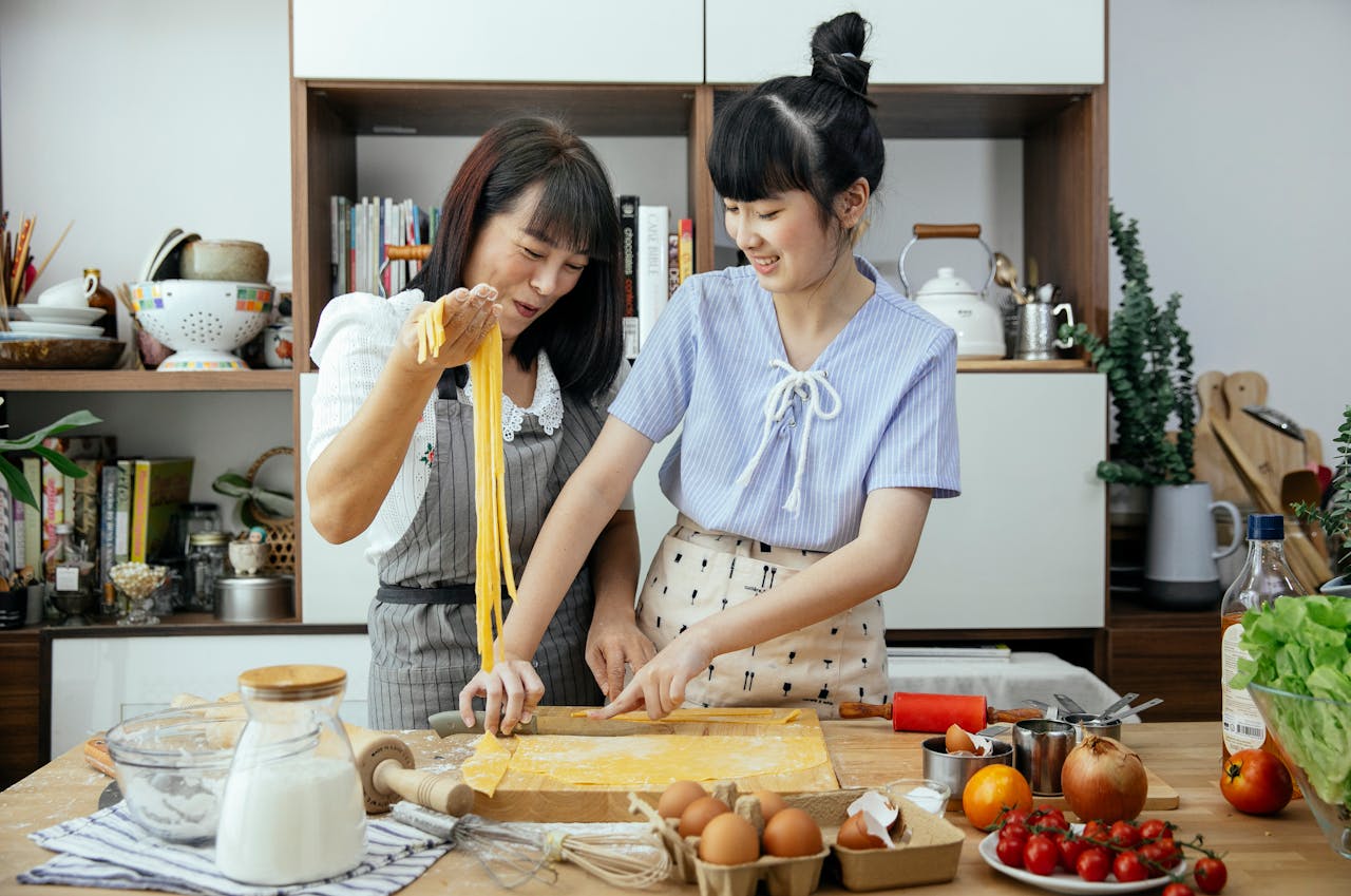 who-we-are A joyful mother and daughter prepare homemade pasta together in the kitchen.